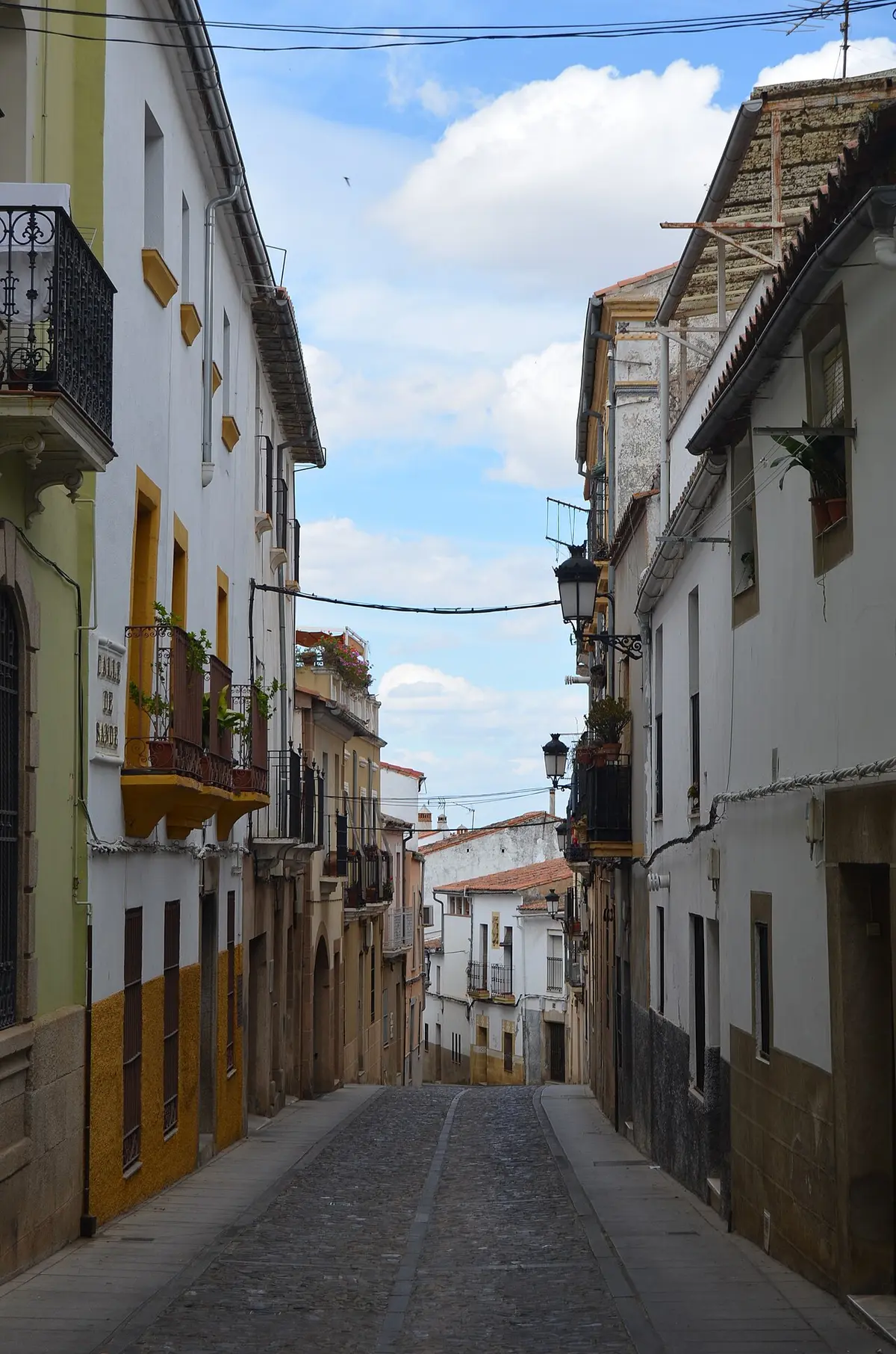 Calle estrecha de casas encaladas en Cáceres, vacía y con el empedrado en cuesta.
