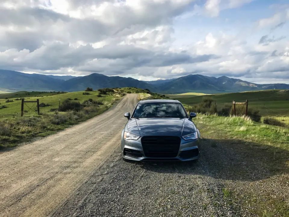 Berlina gris parada en un camino de tierra con montañas al fondo