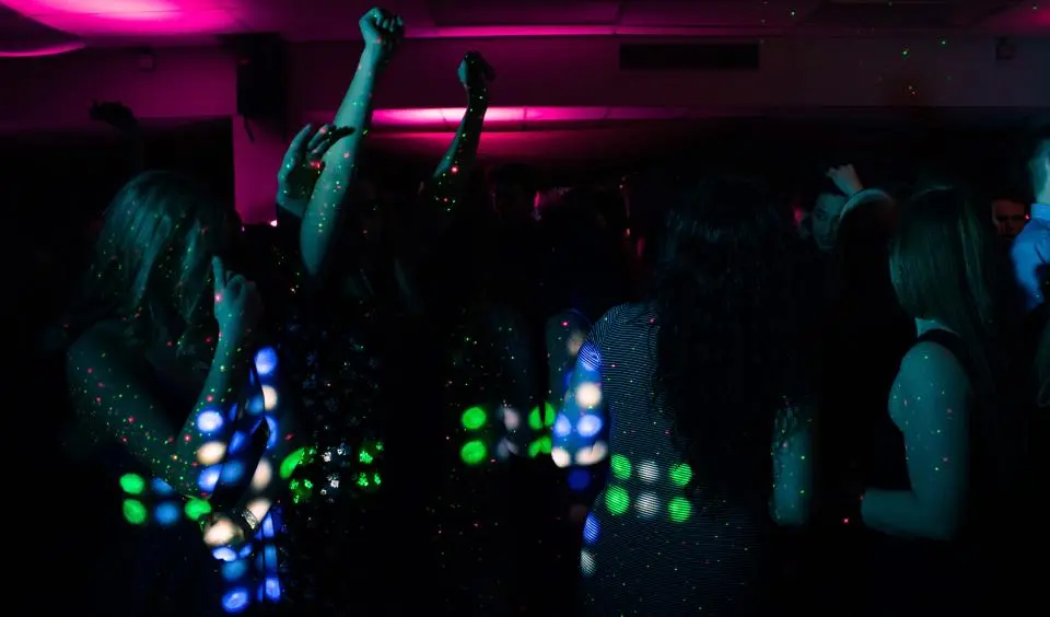 Gente bailando a oscuras con luces de colores en la ropa