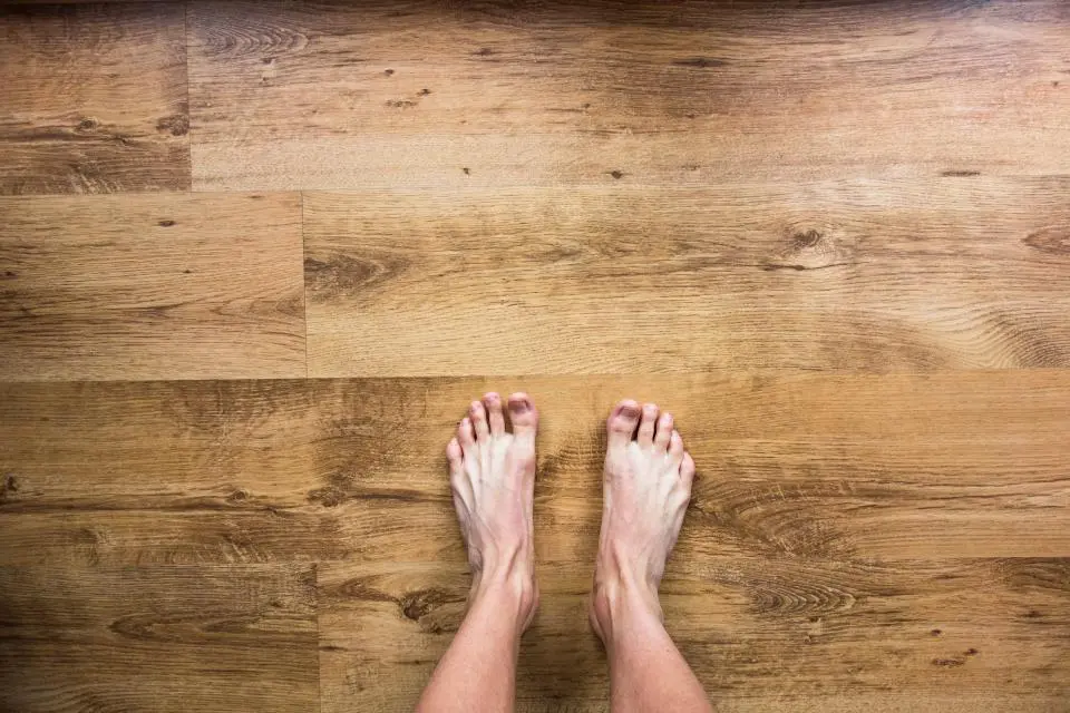 Dos pies descalzos sobre un suelo de madera clara.