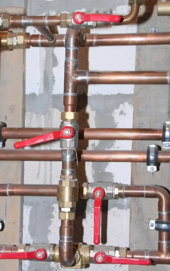 Tuberías de cobre en una pared con varias llaves de paso de palanca roja.