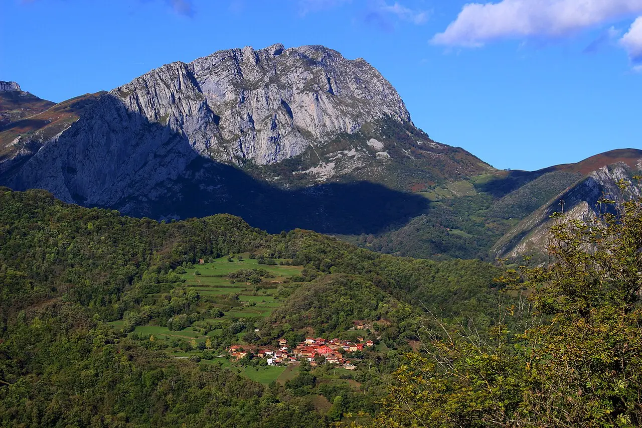 Aldea pequeña entre prados al pie de una gran peña caliza