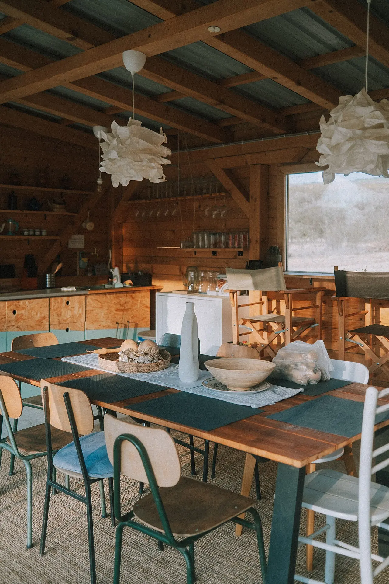 Cocina rústica con vigas de madera, estanterías con cacharros y una mesa larga