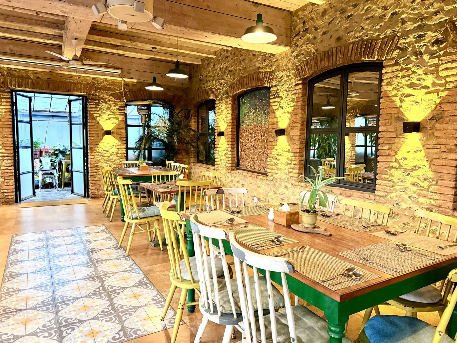 Comedor con paredes de piedra, vigas de madera y una mesa larga con sillas de colores