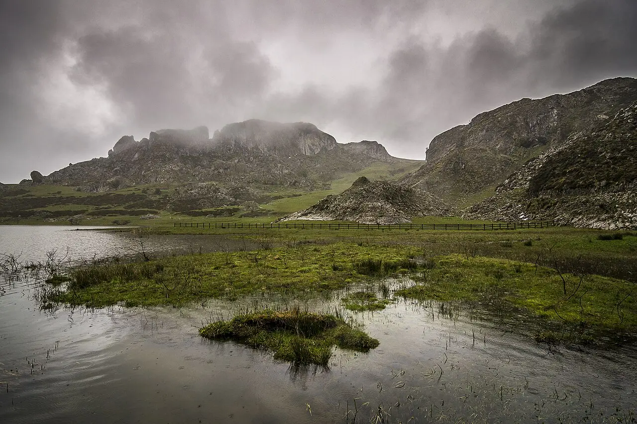 Lago de montaña con niebla baja sobre las peñas y el cielo cubierto