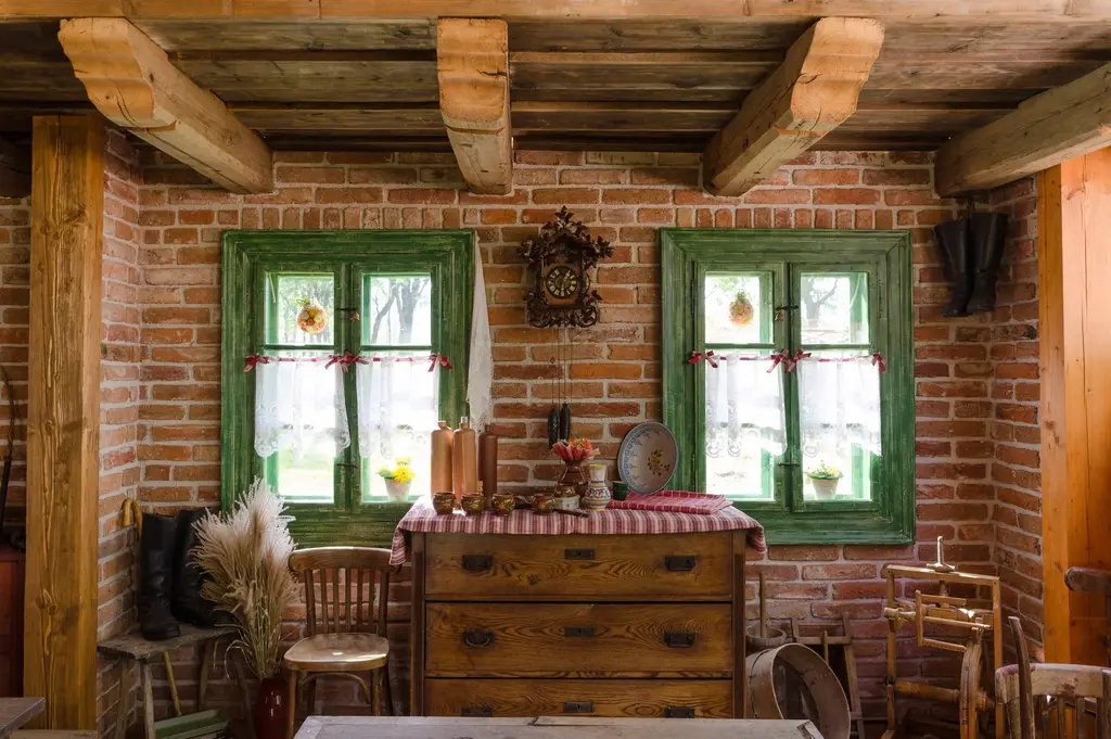 Rincón con vigas de madera, pared de ladrillo, dos ventanas verdes con visillos y una cómoda antigua