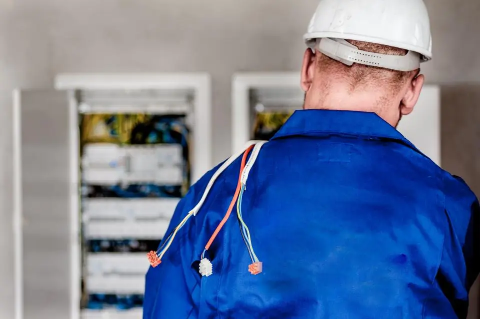 Técnico de espaldas, con casco blanco, delante de dos cuadros eléctricos abiertos