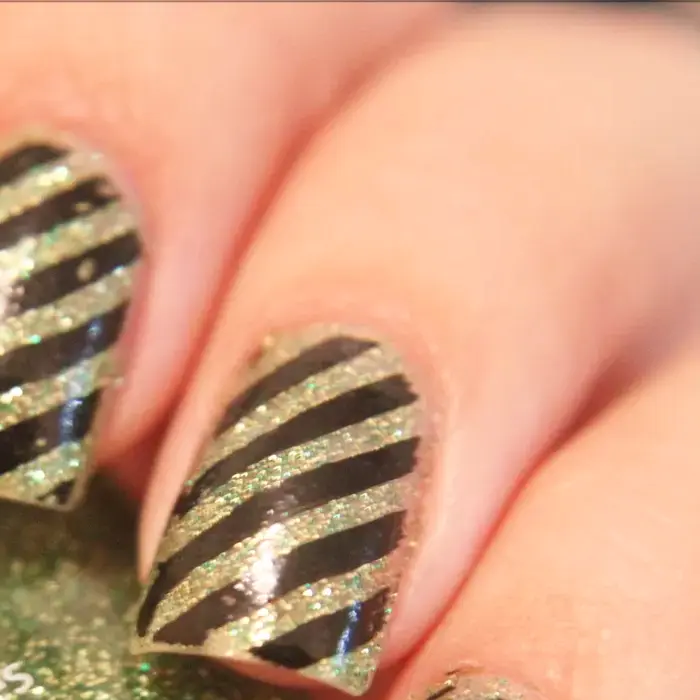 Uñas con purpurina dorada y rayas negras en diagonal