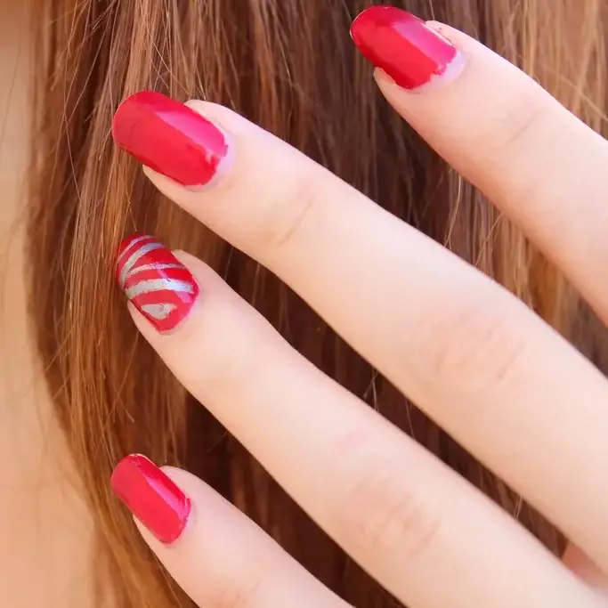 Uñas rojas con una uña de rayas blancas