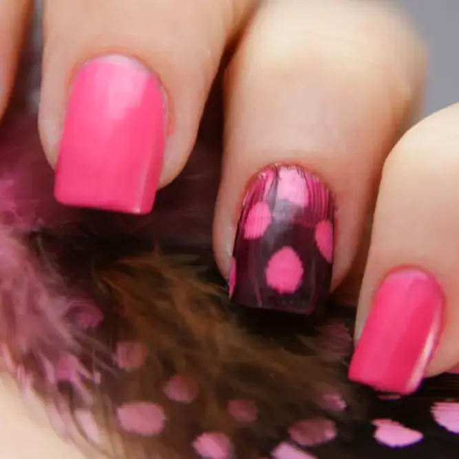 Uñas rosa chicle con una uña de lunares sobre una pluma