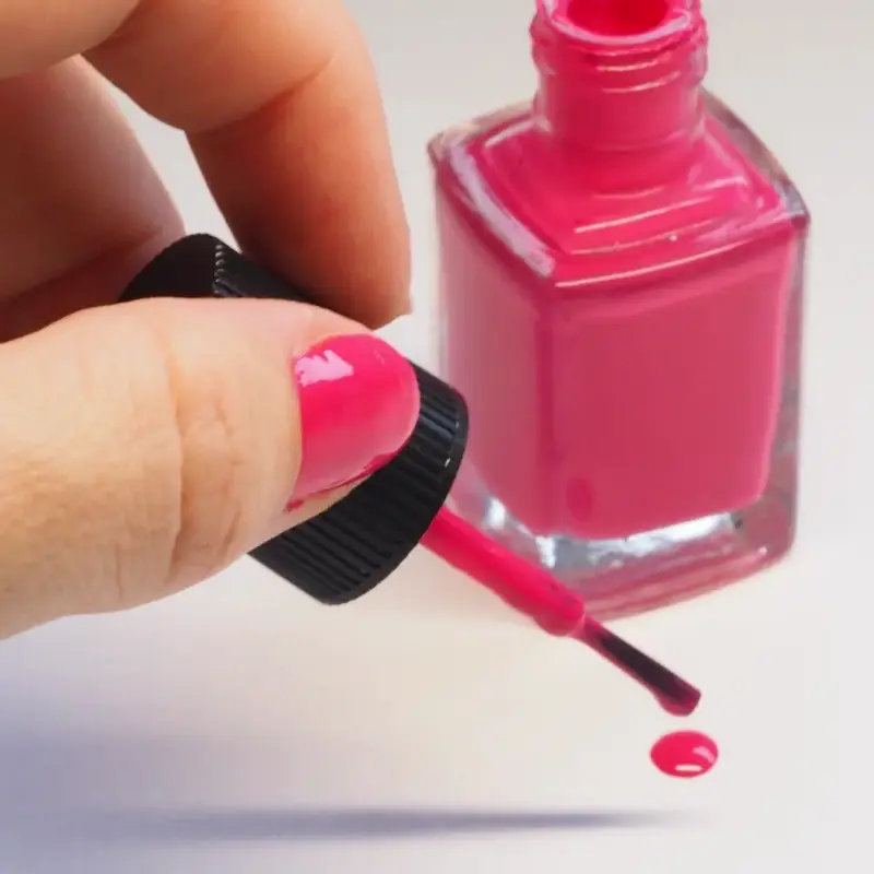 Pincel de esmalte fucsia goteando junto al bote